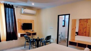 Una habitación de hotel con cama, escritorio con silla, televisor y zona de ducha.