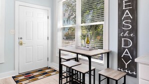 A room with a white door, a window with blinds, a table with two stools, and a wall with the text "SEAS THE DAY".