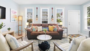 A living room with a brown sofa, two armchairs, a coffee table, and a TV on the wall.