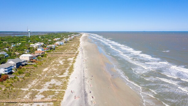 A beach with houses along the shore, a clear sky, and a water tower in the distance.