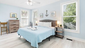 A bedroom with a bed, a dresser, a chair, a nightstand, and a window with blinds.
