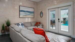 Een moderne woonkamer met een grijze bank, een groot schilderij en uitzicht op een zwembad door glazen deuren.