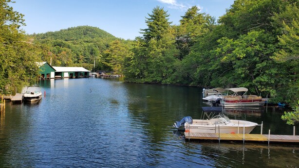A calm river with boats docked at a wooden pier, surrounded by dense forest and a small green building. - In-town Couples Getaway with Dockslipl (Holderness)