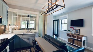A modern kitchen with a built-in island, a dining area with a bench, and a living room with a sofa and TV. - In-town Couples Getaway with Dockslipl (Holderness)