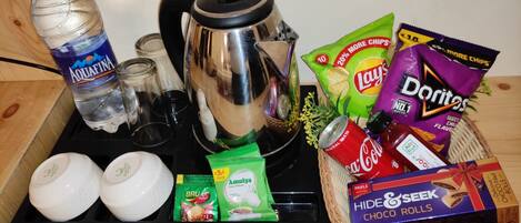 A kitchen counter with a kettle, cups, a bottle of water, snacks, and a box of chocolate rolls.