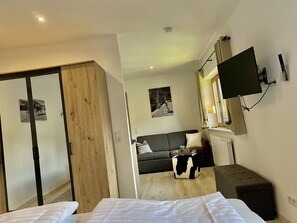 Een hotelkamer met een bed, een slaapbank, een aan de muur bevestigde televisie en een houten garderobe.