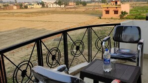 Un balcon avec deux chaises et une table, donnant sur un paysage rural composé de champs et de bâtiments.