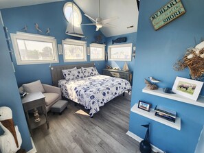 Ein Schlafzimmer mit Bett, Schreibtisch, Stuhl, Deckenventilator und einer Wand mit Dekoration.