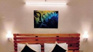 Ein Hotelzimmer mit einem hölzernen Kopfteil, zwei schwarz-weißen Kissen, einer weißen Tagesdecke und einem Bild an der Wand.