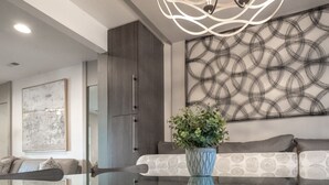 A modern living room with a glass coffee table, grey sofa, abstract wall art, and a decorative plant.