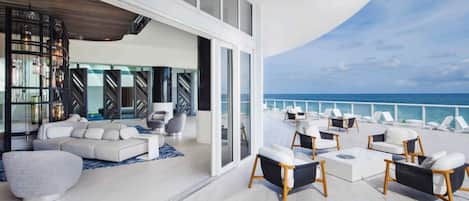 Relax on the spacious balcony overlooking the ocean, surrounded by a seating area and a bookshelf.