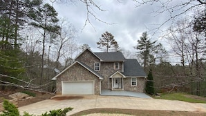 A two-story house with a stone facade, a garage, and a driveway leading to the entrance. - Private Mountain Home in Gated River Resort with Lots of Amenities  (Ellijay)