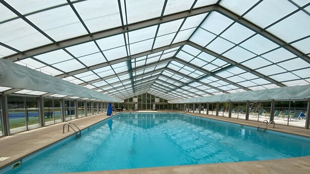 An indoor swimming pool with a glass ceiling, surrounded by lounge chairs and a view of a tennis court. - Private Mountain Home in Gated River Resort with Lots of Amenities  (Ellijay)