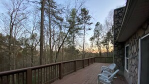A wooden deck with a railing, a rocking chair, and a stone building in the background. - Private Mountain Home in Gated River Resort with Lots of Amenities  (Ellijay)
