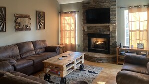 A living room with a stone fireplace, leather sofas, a wooden coffee table, and a mounted TV. - Private Mountain Home in Gated River Resort with Lots of Amenities  (Ellijay)