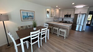 Eine moderne Küche mit weißen Schränken, einem Edelstahl-Kühlschrank und einem Essbereich mit Holztisch und weißen Stühlen.