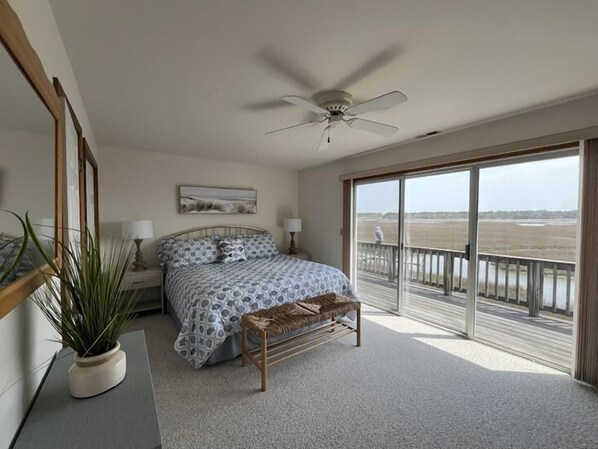 Un dormitorio con cama, ventilador de techo, ventana grande y vista hacia un cuerpo de agua.