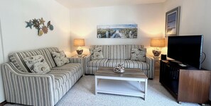 A living room with striped sofas, a coffee table, lamps, a TV, and decorative wall art. - The View-Waterfront w/ Shared Crabbing Pier (Chincoteague)