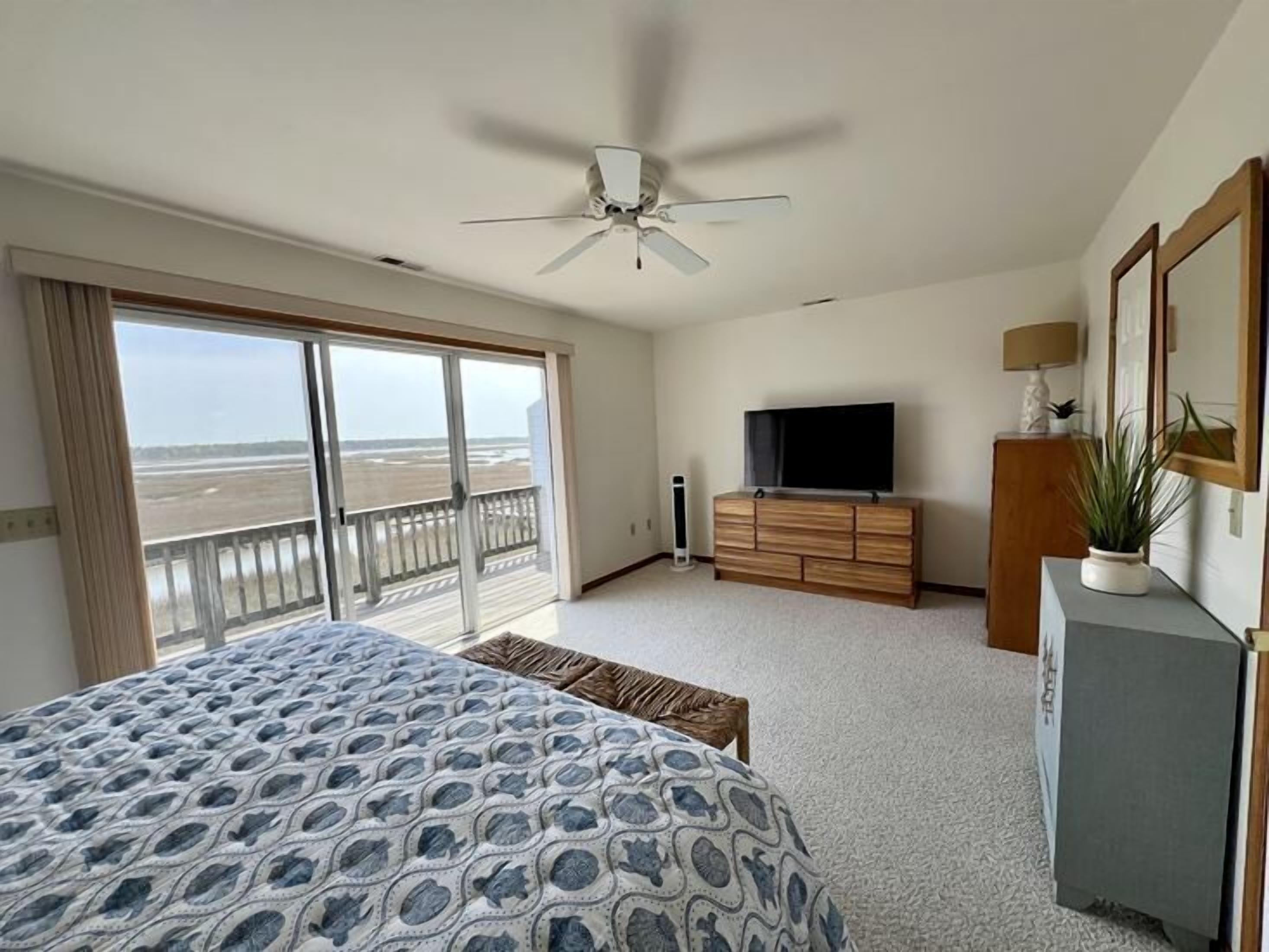 Een slaapkamer met een groot bed, een plafondventilator, een televisie en uitzicht op het strand door de openslaande balkondeuren.