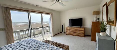 Een slaapkamer met een groot bed, een plafondventilator, een televisie en uitzicht op het strand door de openslaande balkondeuren.