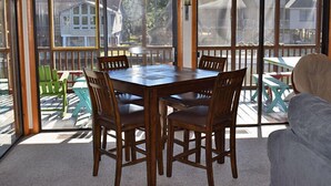 Une terrasse ensoleillée avec une table et des chaises en bois, un canapé confortable et une vue sur les maisons à travers de grandes fenêtres.
