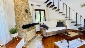 Una sala de estar acogedora con una chimenea de piedra, un sofá, una mesa de centro y una escalera.