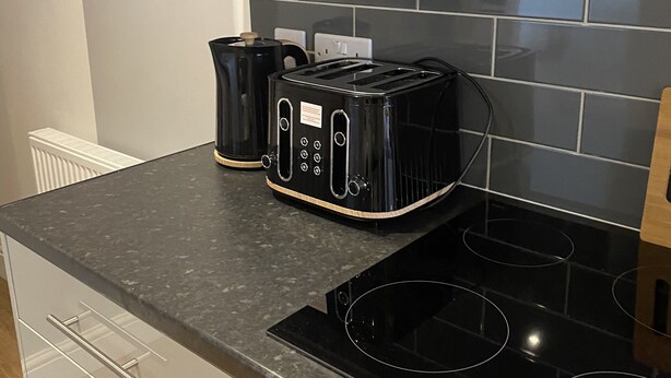A kitchen with a black countertop, a stove, and two black toasters. - Large 3 bed House Sleep 10 Anfield Liverpool (Liverpool)
