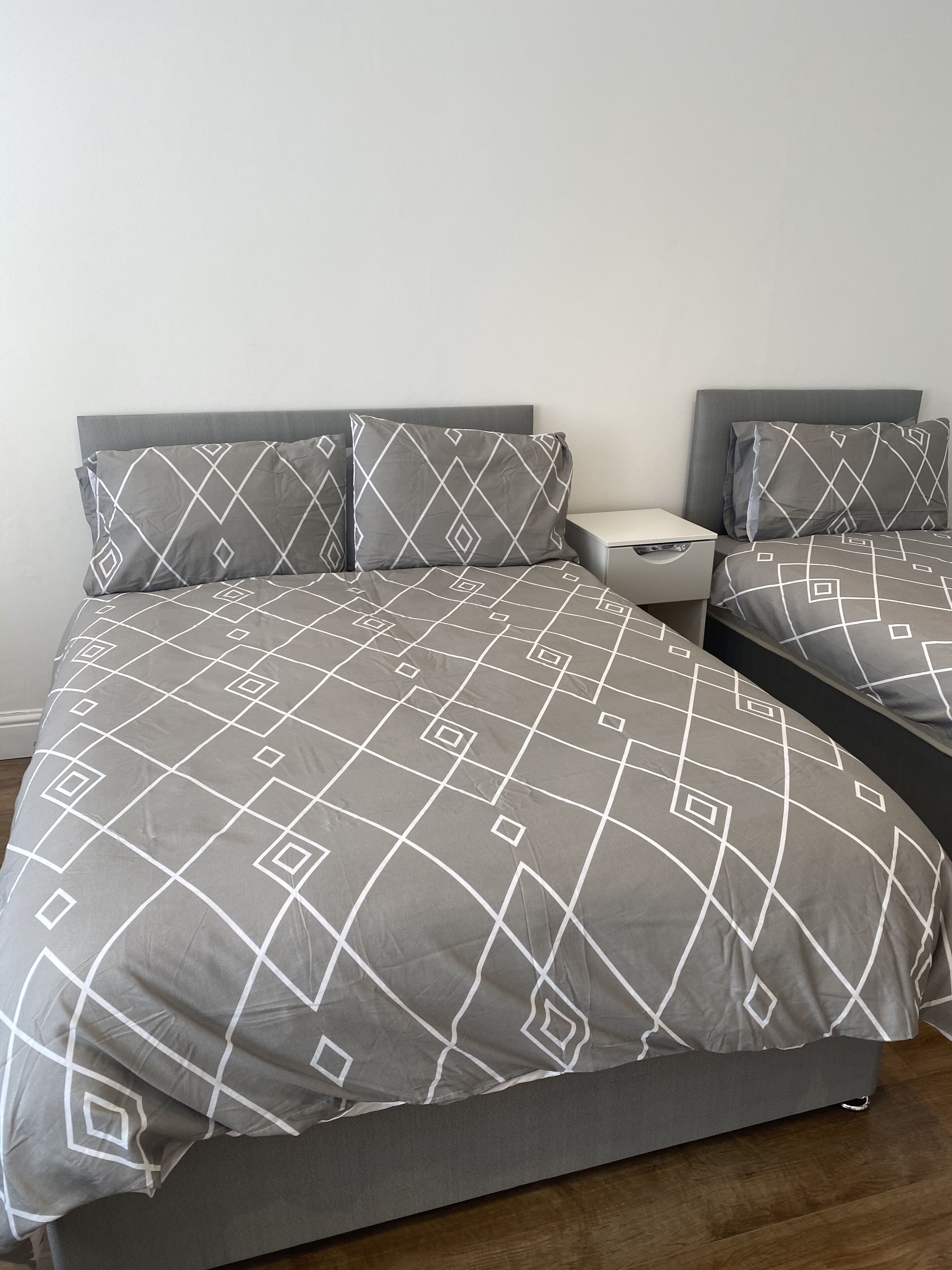 A bed with a geometric patterned bedspread and matching pillows, a bedside table with a lamp, and a wooden floor.