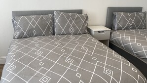 A bed with a geometric patterned bedspread and matching pillows, a bedside table with a lamp, and a wooden floor. - Large 3 bed House Sleep 10 Anfield Liverpool (Liverpool)