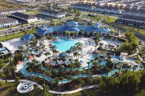 An aerial view of a resort with multiple swimming pools, palm trees, and a large building with a blue roof.