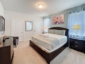 A bedroom with a large bed, a desk, a dresser, and a window with blinds.