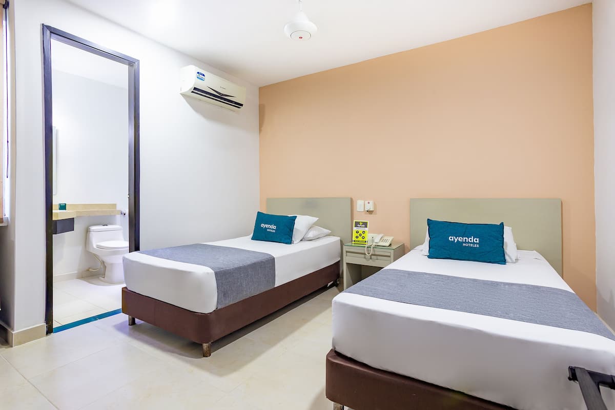 Een hotelkamer met twee bedden, een badkamer en een klein bureau met telefoon.