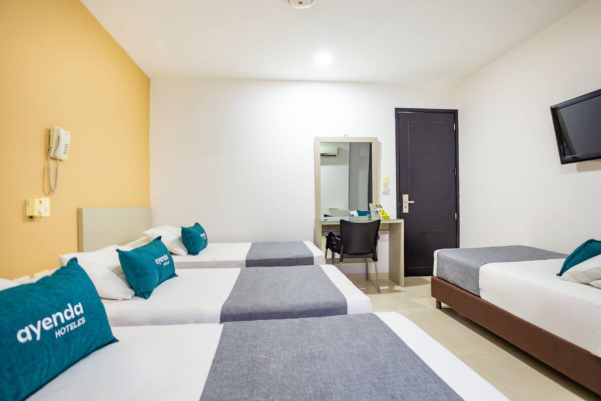 Hotelkamer met drie bedden, een bureau, een stoel, een televisie en een telefoon.