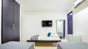 A hotel room with two beds, a TV, a mirror, a wardrobe, and a small refrigerator.