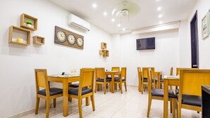 A dining area with wooden tables and chairs, a wall-mounted clock, and an air conditioning unit.