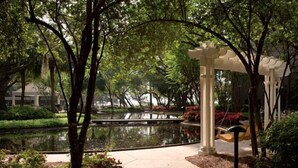 Un jardí tranquil amb un estany, una pèrgola blanca i un camí.