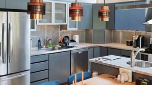 A modern kitchen with stainless steel appliances, a wooden dining table, and pendant lights. - Tin Cup Palace- Community Boat Launch, Fire Pit & Screened Porch (Chincoteague)