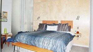 A bedroom with a bed, bedside tables, a bench, a ceiling fan, and a window with blinds. - Tin Cup Palace- Community Boat Launch, Fire Pit & Screened Porch (Chincoteague)