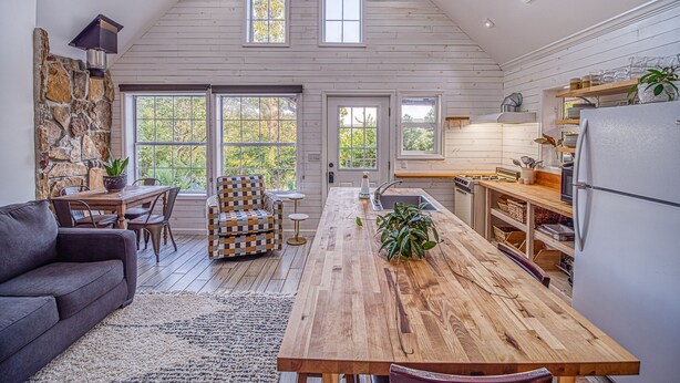 Un'ampia cucina in stile loft con soffitto alto, grandi finestre e zona pranzo con tavolo e sedie in legno.