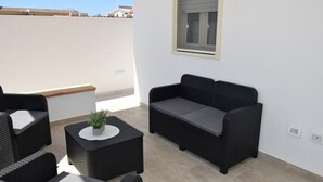 A rooftop patio with a black wicker sofa, two wicker chairs, and a small round table with a plant. - A stone's throw from the sea (Santa Maria del Focallo Ispica)