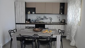 A modern kitchen with a marble backsplash, a dining table with chairs, and a kitchen island with a sink and countertop. - A stone's throw from the sea (Santa Maria del Focallo Ispica)