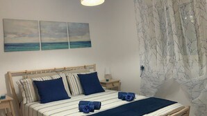 A neatly made bed with a striped bedspread and blue pillows, a bedside table with a lamp, and a view of the sea through the window. - A stone's throw from the sea (Santa Maria del Focallo Ispica)