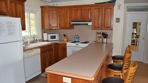 Eine Küche mit Holzschränken, einem weißen Kühlschrank, einer Mikrowelle, einem Herd und einer Bar mit Sesseln.