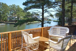 A wooden deck with wicker furniture overlooking a calm lake, surrounded by trees and houses. - Topaz- Canalfront with Boat Dock (Chincoteague)