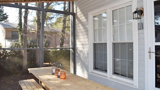 Une terrasse couverte avec une table et des bancs en bois, une fenêtre donnant sur des maisons et une lanterne fixée au mur.