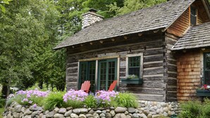 Eine rustikale Holzhütte mit steinernen Fundament, Holzläden und einem Steinkamin.