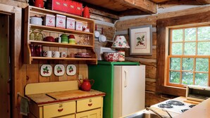 Eine rustikale Küche mit Holzwänden, Holzbalkendecke, einem weißen Kühlschrank, einem Herd sowie verschiedenen Küchenutensilien und Geschirr.