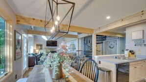 A modern kitchen with a central island, wooden beams, and a dining area with a long table and chairs.