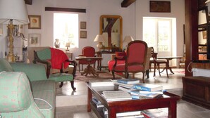 Una sala de estar acogedora con chimenea, vigas de madera, un sillón verde, un sillón rojo y una mesa de centro con libros.