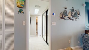 A hallway with a door leading to a room, a wall with decorative sailboat models, and a patterned chair.